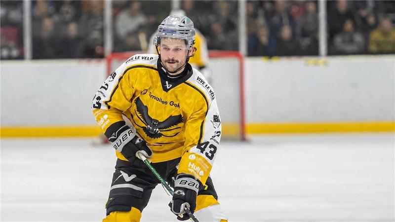 Eishockeyspieler in gelb-schwarzer Ausrüstung mit Helm und Stock auf dem Eis vor dem Tor