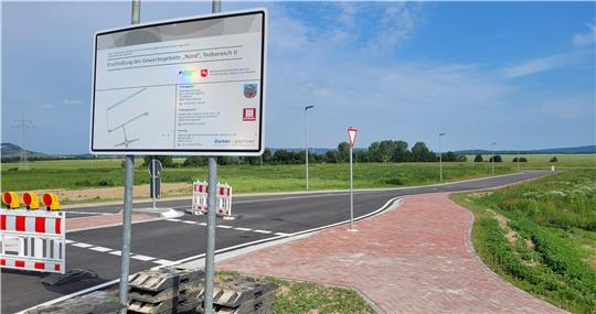 Ein Baustellenschild und im Hintergrund eine frisch fertiggestellte Straße, die über ein unbebautes Feld führt.