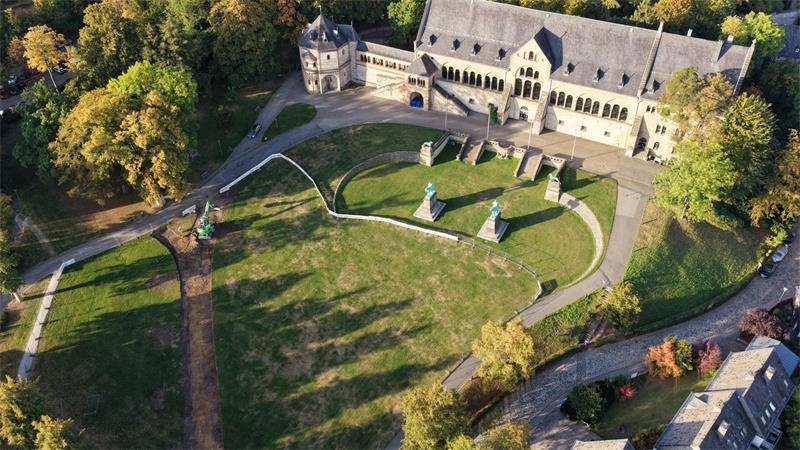 Luftaufnahme eines historischen Gebäudes mit angrenzendem Park und mehreren Statuen auf einer Rasenfläche.
