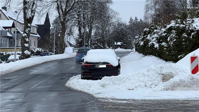 Ein verschneites Auto steht in einer verschneiten Straße.