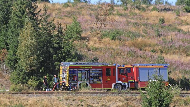Einsatzkräfte der Feuerwehr stehen am Waldrand nahe Benneckenstein und halten die Wasserversorgung aufrecht.