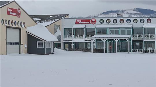 Schneebedeckte Gewerbegebäude mit mehreren runden Firmenschildern an den Fassaden und bewölktem Himmel im Hintergrund.