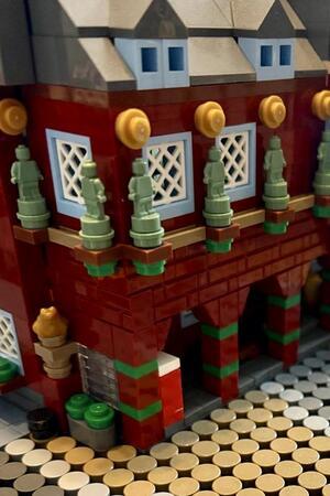 Detailaufnahme eines roten Lego-Gebäudes mit kleinen grünen Figuren auf einem Balkon und grauen Dächern.