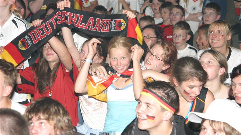 Junge Menschen in einer Menschenmenge mit Deutschland-Schal und schwarz-rot-goldenen Gesichtsbemalungen feiern ausgelassen