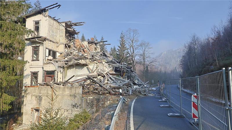 Teilweise eingestürztes mehrstöckiges Gebäude neben einer kurvigen Straße mit Absperrung und Wald im Hintergrund