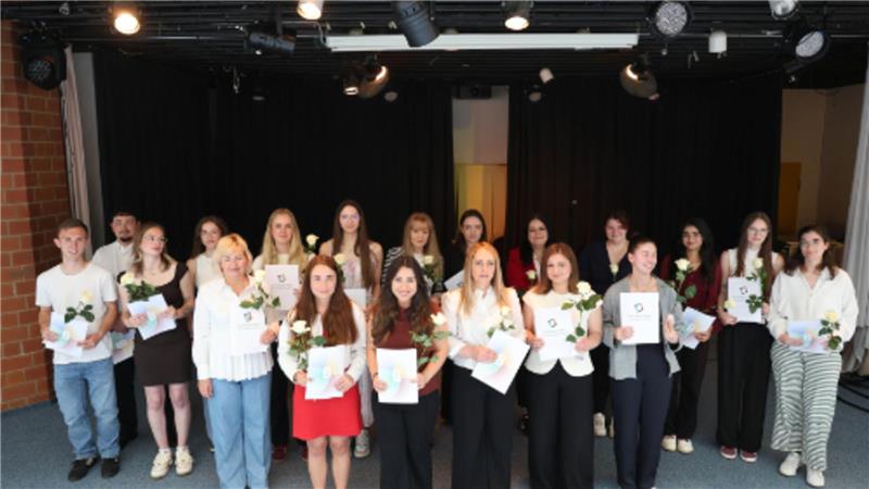 Mehrere Frauen und Männer halten Urkunden und eine Blume in der Hand