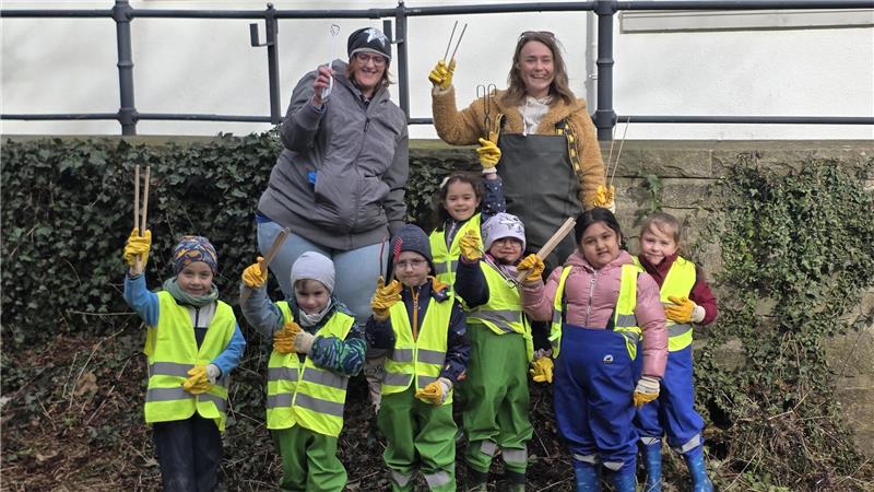 Vom Staubsauger bis zur Wodkaflasche: Müllsammler entdecken Kurioses Gruppe von Kindern mit Warnwesten und Gummistiefeln steht vor einer Mauer, zwei Erwachsene mit Handschuhen und Greifzangen heben die Hände.