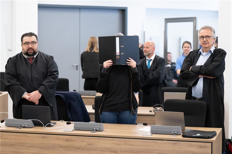 Gericht verurteilt mutmaßliche Linksextremisten – Proteste im Saal Die Angeklagte (M) steht bei der Fortsetzung des Prozesses im Oberlandesgericht (OLG) Dresden im Verhandlungssaal und hält einen Aktenordner vor ihr Gesicht. Die Gruppe bestehend aus Lina E. und drei Männern aus der linksextremistischen Leipziger Szene ist wegen Mitgliedschaft in einer kriminellen Vereinigung angeklagt. Foto: Sebastian Kahnert/dpa