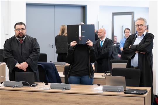 Die Angeklagte (M) steht bei der Fortsetzung des Prozesses im Oberlandesgericht (OLG) Dresden im Verhandlungssaal und hält einen Aktenordner vor ihr Gesicht. Die Gruppe bestehend aus Lina E. und drei Männern aus der linksextremistischen Leipziger Szene ist wegen Mitgliedschaft in einer kriminellen Vereinigung angeklagt. Foto: Sebastian Kahnert/dpa