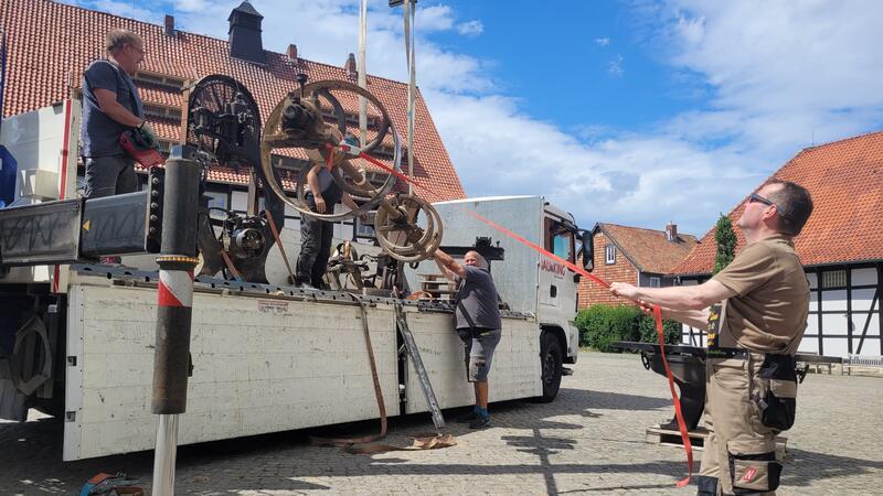 Ein schweres Maschinenteil wird per Kran von einem Lastwagen gehievt.