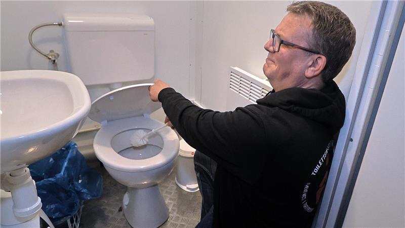 GZ-Redakteur Sowa im WC-Einsatz: Zwischen Klobürste und Flatrate Ein Mann in schwarzem Kapuzenpullover schrubbt mit der Klobürste die Toilette in einem kleinen Zimmer.