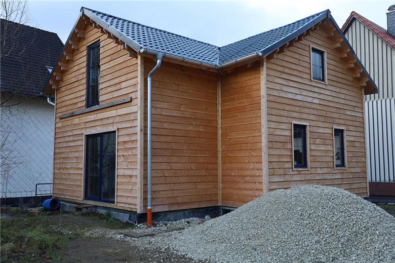 Holzhaus mit Satteldach, mehreren Fenstern und einer großen Glastür, daneben ein großer Kieshaufen