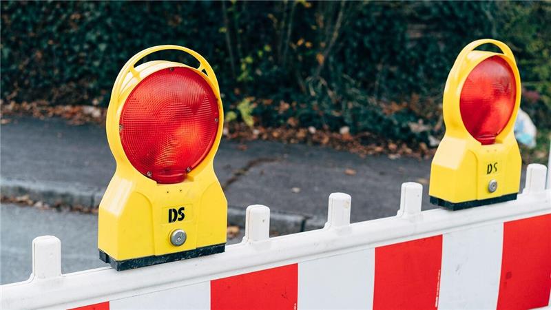 Gelbe Warnleuchten mit roten Reflektoren auf einer rot-weißen Absperrung im Freien
