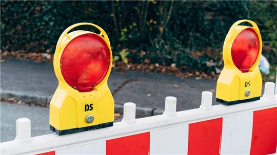 Gelbe Warnleuchten mit roten Reflektoren auf einer rot-weißen Absperrung im Freien