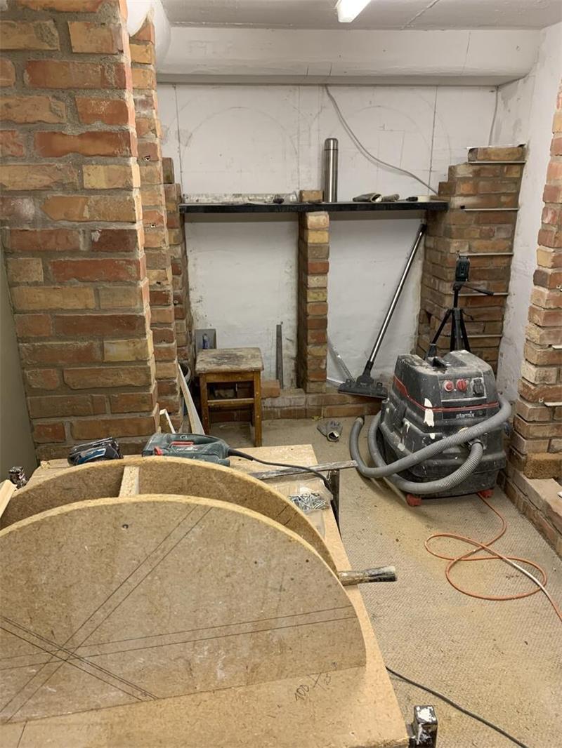 Baustelle mit freigelegten Ziegelwänden, Baugeräten und einem großen runden Holzstück im Vordergrund