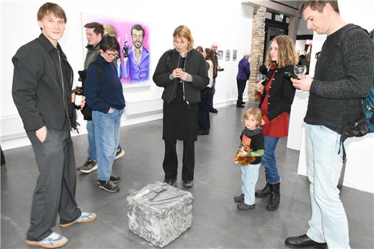Junge Menschen und ein Kind stehen um einen Stahlblock herum, der auf dem grauen Fußboden eines Ausstellungsraumes steht.