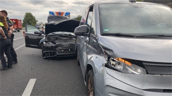 Ein schwarzes Auto mit offenen Türen und offener Motorhaube steht hinter einem silbernen Van. Beide Fahrzeuge sind beschädigt. Daneben stehen Polizisten.