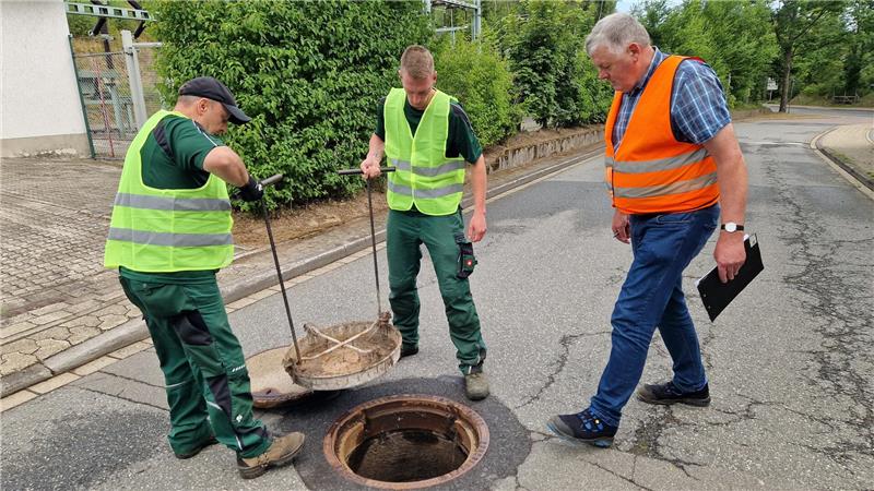 Die Bauhofmitarbeiter der Kurbetriebsgesellschaft (v.l.) Matthias Schwarz und Kevin Schmitz öffnen die Gullys in Altenau. Helmut Jacobs vom Landesamt für Verbraucherschutz und Lebensmittelsicherheit sucht nach möglichen Rattenspuren.