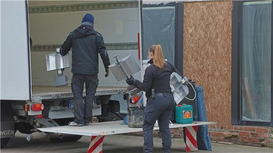 Die Beamten tragen mehrere Geräte und Säcke aus dem betroffenen Gebäude.