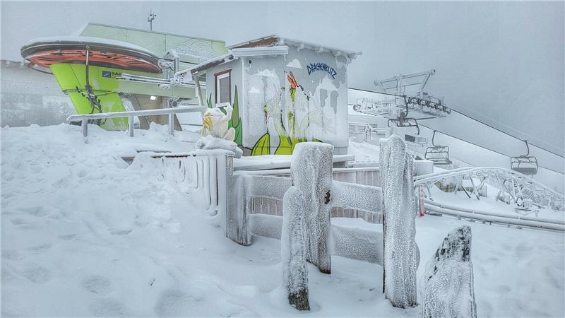 Verschneite Skistation mit Sessellift und vereisten Holzzäunen unter bewölktem Himmel.