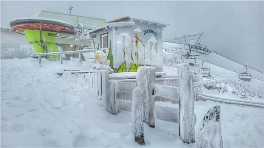 Verschneite Skistation mit Sessellift und vereisten Holzzäunen unter bewölktem Himmel.