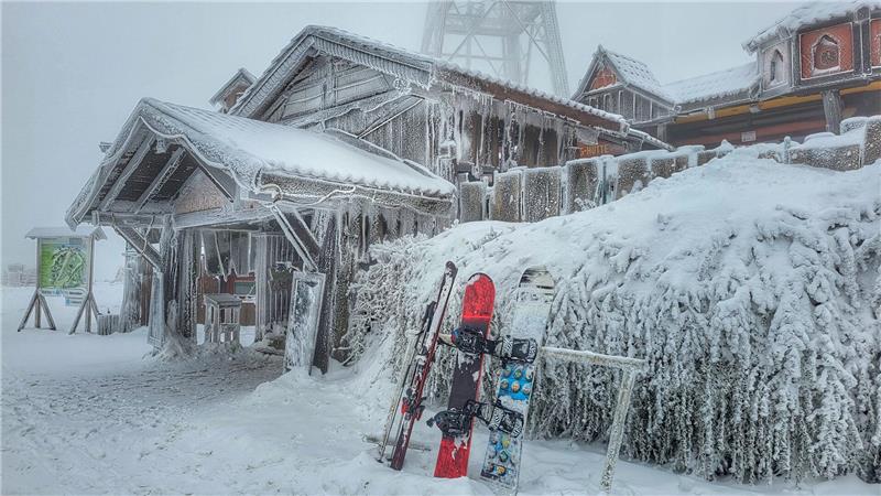 Schneebedecktes Holzgebäude mit Skiern und Snowboard, die an einem Geländer lehnen, im Nebel.