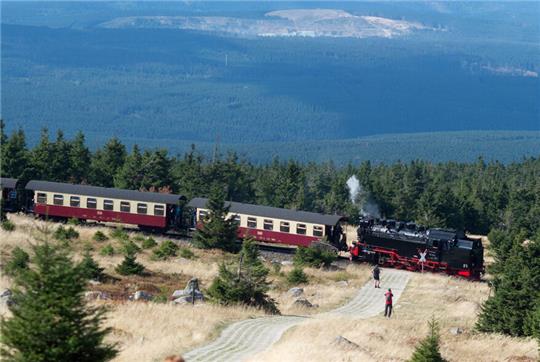 Die Brockenbahn der Harzer Schmalspurbahnen verlässt bei ruhigem, spätsommerlichem Wetter das Gipfelplateau und fährt Richtung Tal, während Wanderer einen alte Patrouillenweg hoch gehen. (Symbolbild)