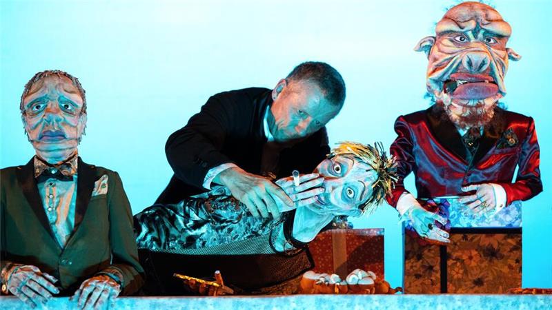 Ein Mann steht hinter drei lebensgroßen Figuren. Die mittlere liegt und hat eine Zigarette in der Hand.