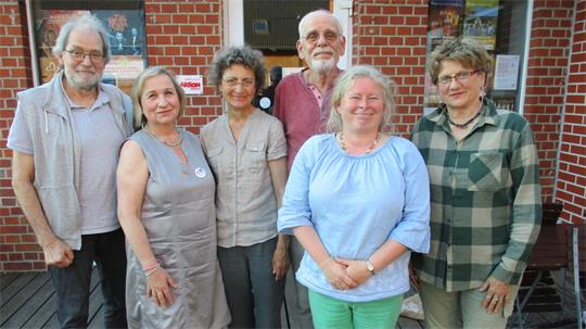 Sechs Personen stehen nebeneinander vor einem Backsteingebäude und lächeln in die Kamera