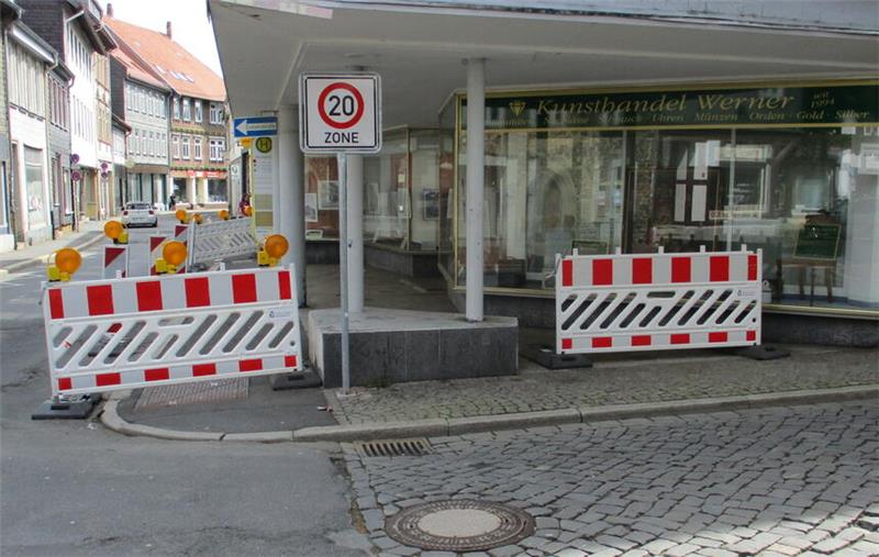Absperrungen mit rot-weißen Streifen und Warnleuchten blockieren einen gepflasterten Gehweg vor einem Geschäft mit Glasfront und Säulen