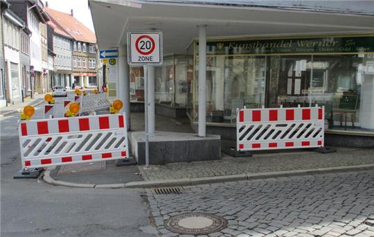 Absperrungen mit rot-weißen Streifen und Warnleuchten blockieren einen gepflasterten Gehweg vor einem Geschäft mit Glasfront und Säulen