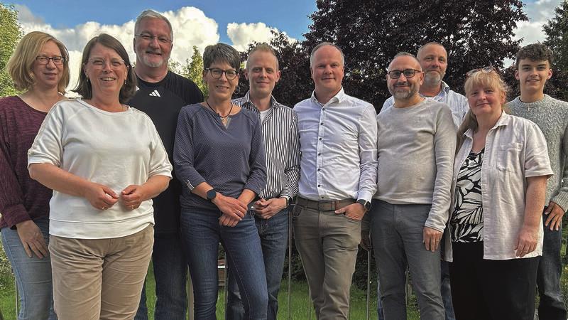 Gruppe von zehn Personen steht im Freien vor grünem Gras und blauem Himmel mit Wolken