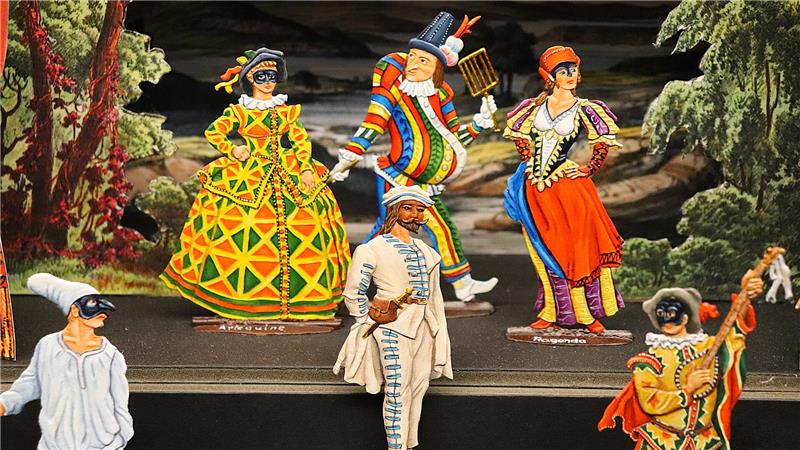 Perücken, Pomp und Pulverdampf im Goslarer Zinnfigurenmuseum Figuren in farbenfrohen historischen Kostümen auf einer Bühne mit Waldkulisse, darunter ein Harlekin, eine Dame im großen Kleid und ein Musiker mit Gitarre