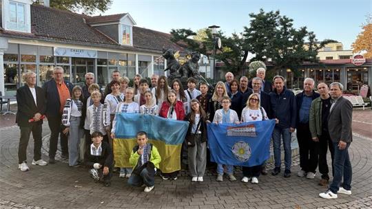 Gruppenfoto von Menschen unterschiedlichen Alters vor einem Gebäude mit Schaufenstern, zwei Personen halten ukrainische und eine weitere Flagge.