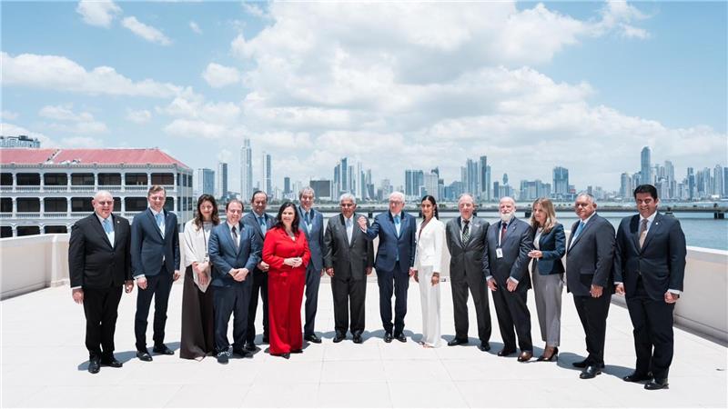 Gruppe von Menschen in formeller Kleidung steht auf einer Dachterrasse mit Stadtpanorama im Hintergrund