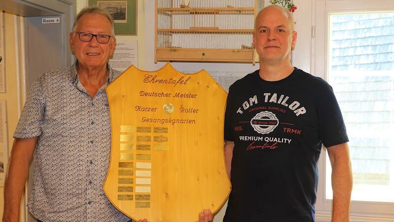 Die Deutschen Meister Ulf Raabe (rechts) und Hans-Jürgen Wohlidka bringen Im Kanarienmuseum die aktuelle Siegerplakette auf der Ehrentafel an.