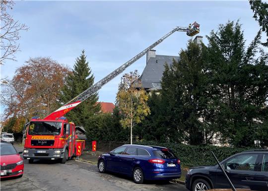 Feuerwehrfahrzeug mit ausgefahrener Drehleiter vor einem mehrstöckigen Wohnhaus in einer Straße mit parkenden Autos.
