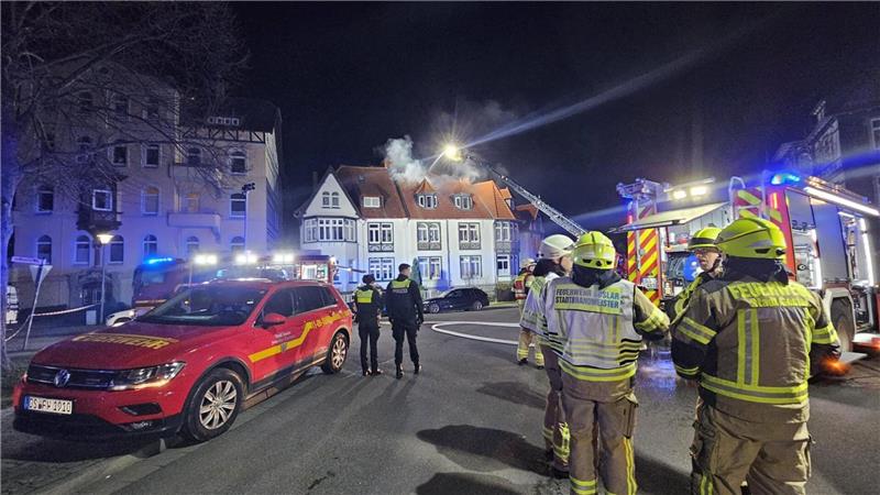 Einsatzkräfte der Feuerwehr und der Polizei stehen vor dem brennenden Haus.