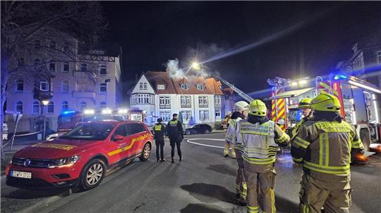 Einsatzkräfte der Feuerwehr und der Polizei stehen vor dem brennenden Haus.