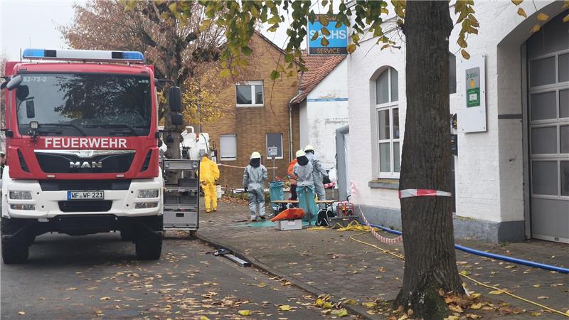 Ein Feuerwehrauto steht am Straßenrand, während daneben die Einsatzkräfte in Schutzanzügen arbeiten.