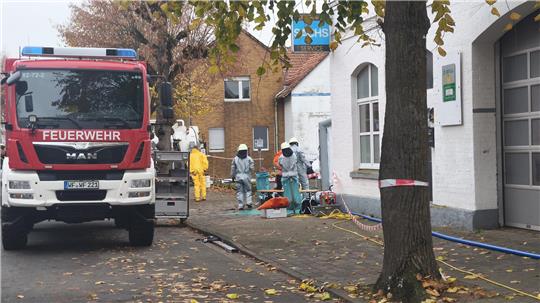 Ein Feuerwehrauto steht am Straßenrand, während daneben die Einsatzkräfte in Schutzanzügen arbeiten.