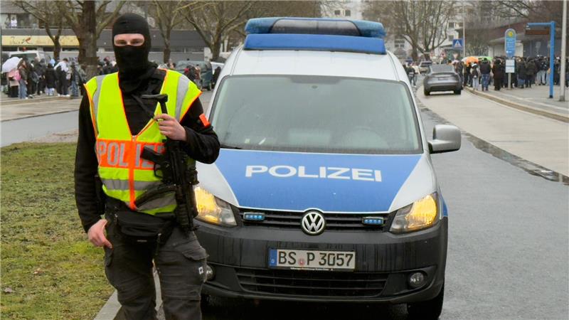 Ein vermumter Polizist steht vor einem Polizeiauto