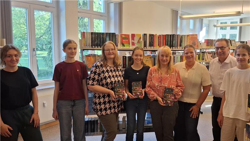 Eine Gruppe von Menschen, drei Personen halten Bücher in der Hand.