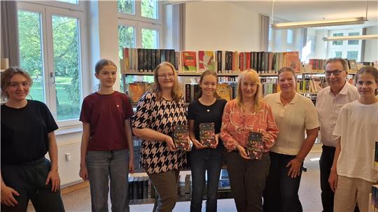 Eine Gruppe von Menschen, drei Personen halten Bücher in der Hand.
