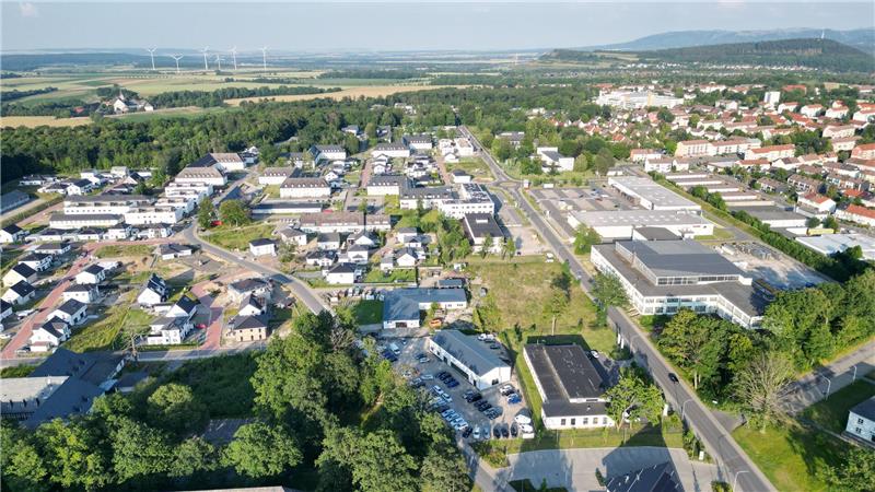 Luftaufnahme einer Kleinstadt mit Wohnhäusern, Gewerbegebäuden, Straßen und Windrädern im Hintergrund