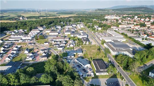 Luftaufnahme einer Kleinstadt mit Wohnhäusern, Gewerbegebäuden, Straßen und Windrädern im Hintergrund