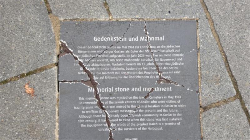 Rissige Gedenktafel aus Stein mit Text zum Gedenkstein und Mahnmal in einem Gehweg