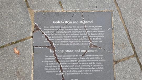 Rissige Gedenktafel aus Stein mit Text zum Gedenkstein und Mahnmal in einem Gehweg