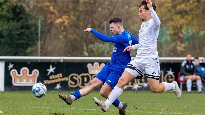 Zwei Fußballspieler in blauer und weißer Sportkleidung treten gleichzeitig nach einem Ball auf einem Rasenplatz