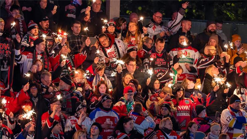 Menschenmenge in Sporttrikots hält Wunderkerzen bei Abendveranstaltung.